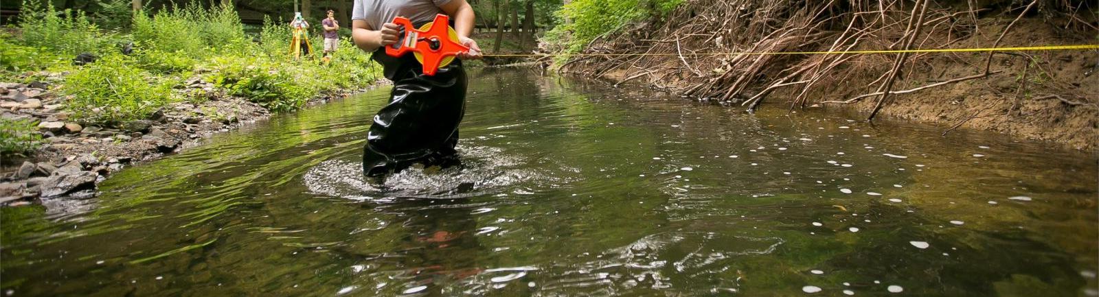 Temple environmental studies student standing in a creek in the woods performing an experiment.